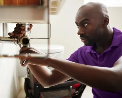 Young black male plumber sitting on the floor fixing a bathroom sink, close up