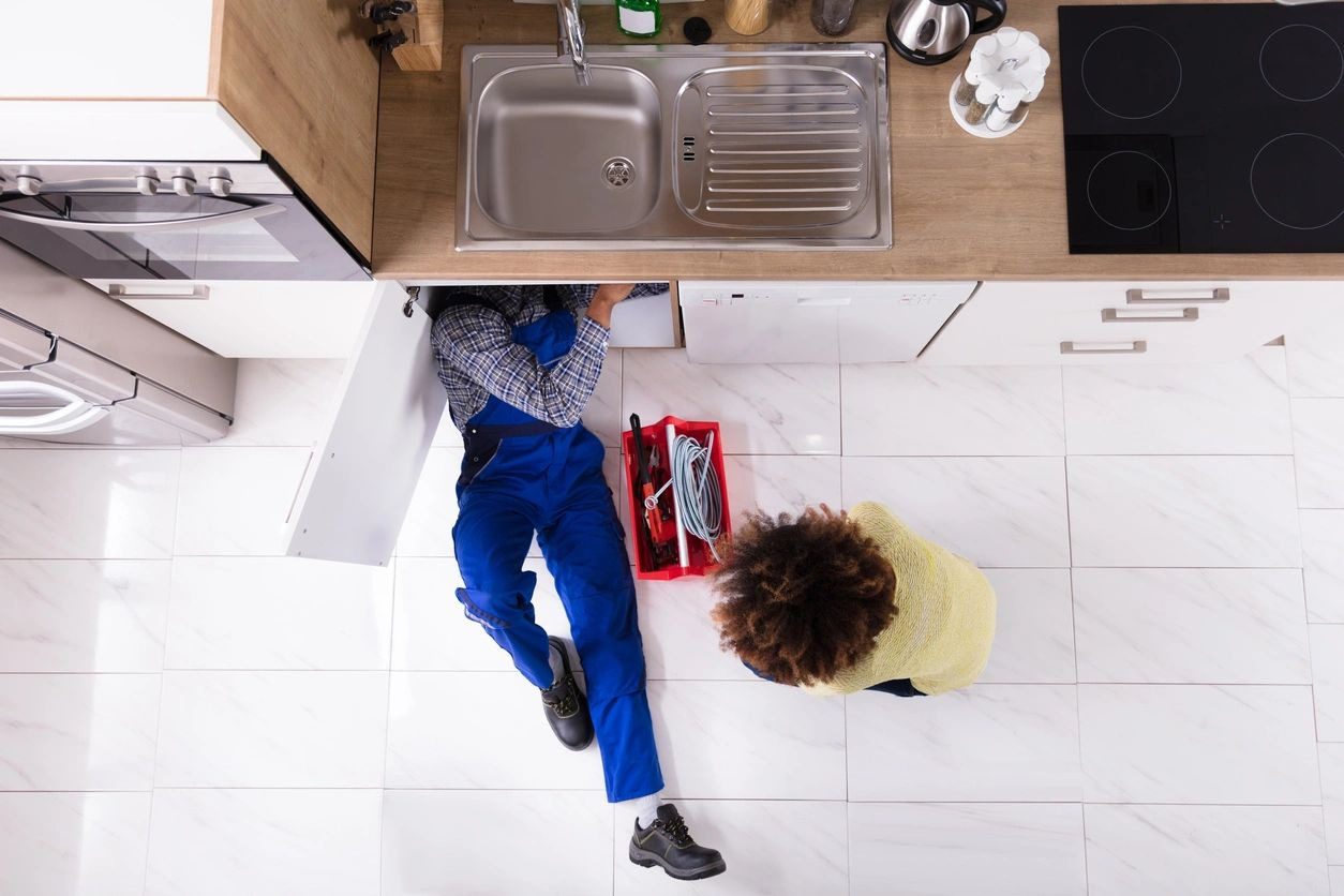 High Angle View Of Woman Looking At Plumber Repairing Sink In Kitchen