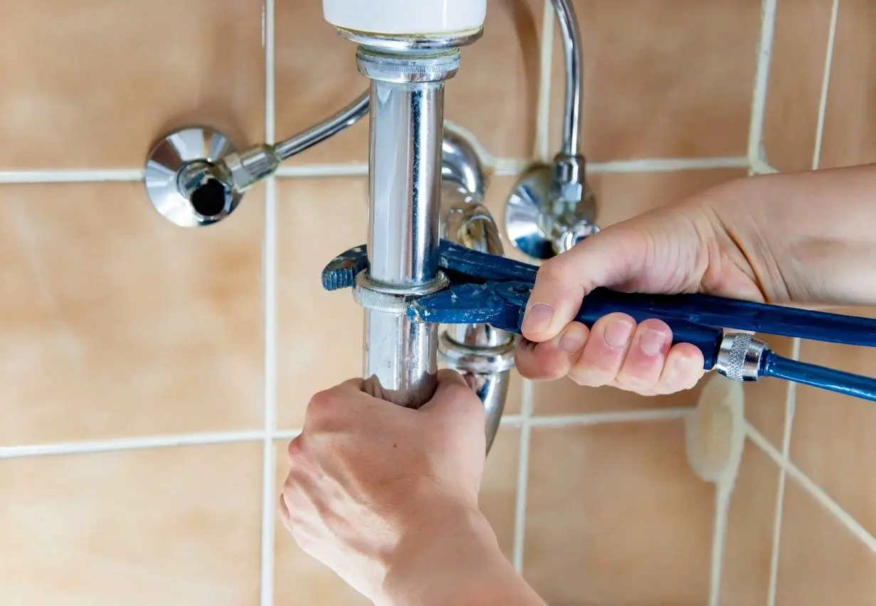 Hands of a plumber with sink and wrench